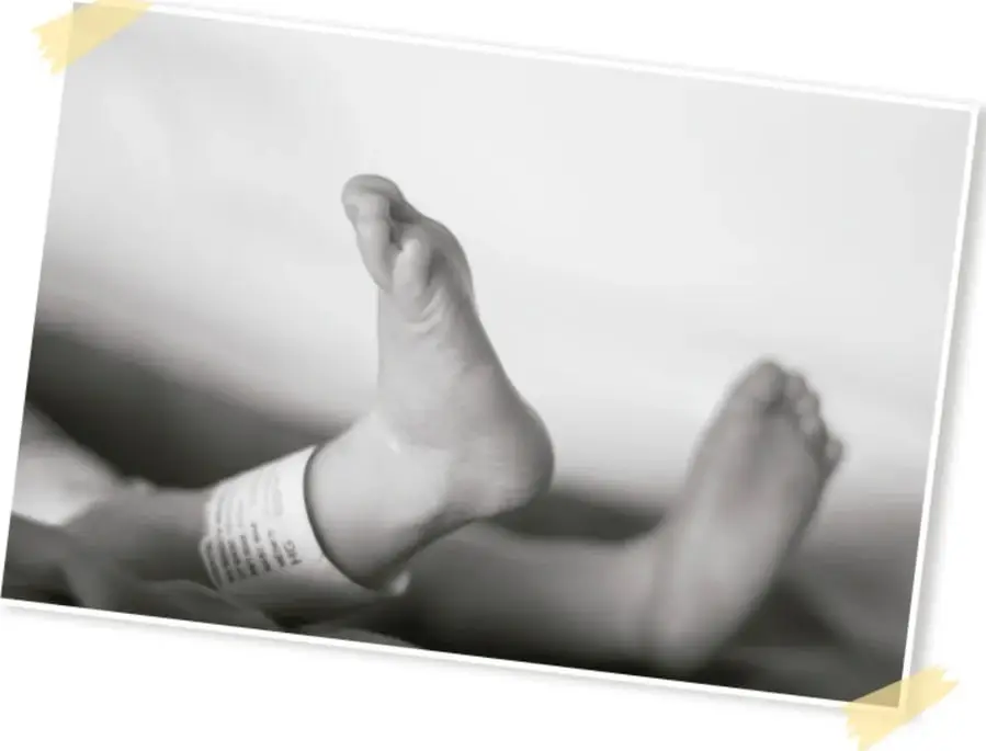 Fotografía en blanco y negro, pegada con cintas adhesivas amarillas, de los pies de un bebé recién nacido; en el tobillo se ve la pulsera de identificación del hospital.