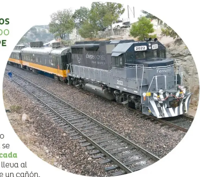 Locomotora gris del Chepe Express (número 2022, Ferromex) tirando de vagones amarillos y grises sobre una curva de vías; un persona camina junto a la vía y al fondo hay árboles y autos.