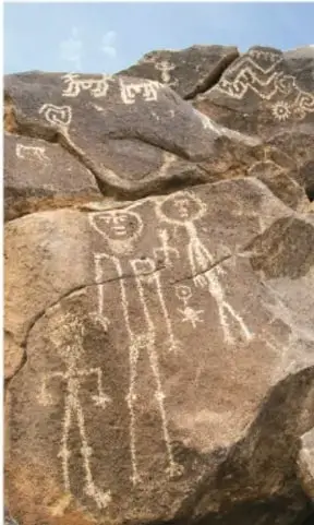 Fotografía de un muro de roca con petroglifos grabados: figuras humanas estilizadas, espirales y signos geométricos, probablemente de la cultura hohokam.