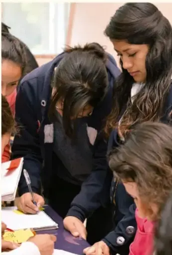 Fotografía de varias estudiantes trabajando juntas sobre una mesa con libros y hojas