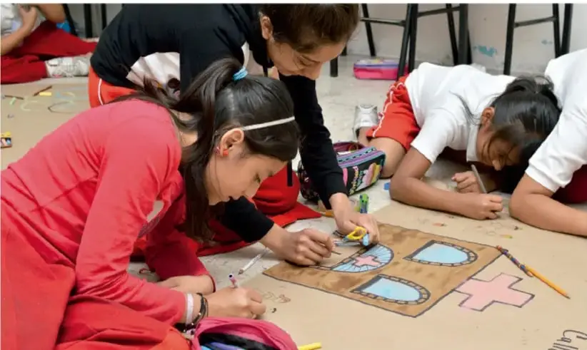 Estudiantes de primaria trabajan en el piso elaborando un periódico mural con cartulinas, dibujos y pegamento.