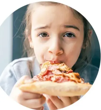 Fotografía circular de una niña comiendo una rebanada de pizza, que ilustra el consumo de alimentos ultraprocesados.