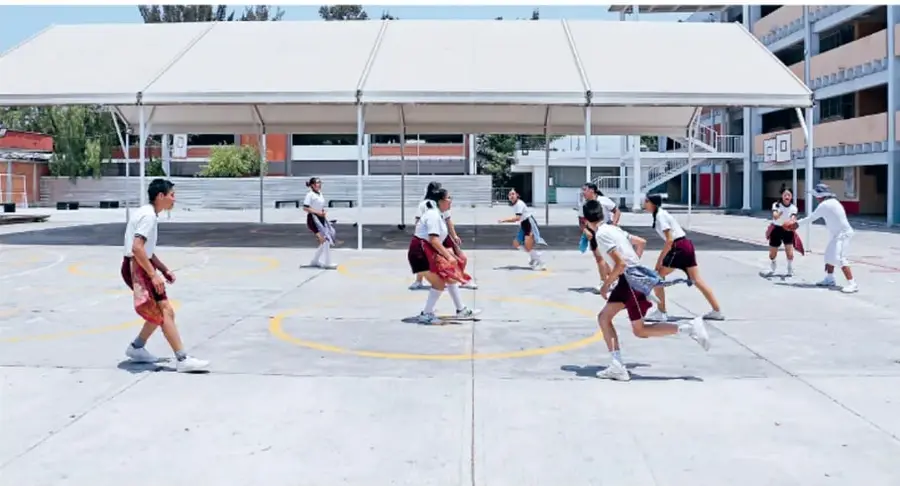 Fotografía de estudiantes de secundaria jugando en un patio escolar techado, realizando una actividad recreativa en círculos pintados en el piso.