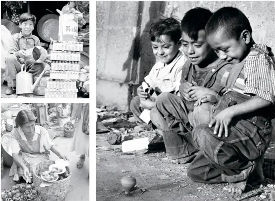 Fotografía en blanco y negro: tres niños jugando con un trompo en la calle, agachados y sonrientes, descalzos sobre la tierra.