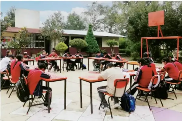 Fotografía de estudiantes de telesecundaria trabajando en equipos con mesas en el patio de su escuela.