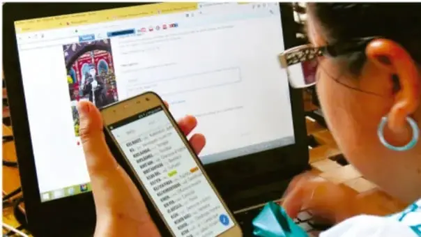 Fotografía de una persona utilizando un teléfono inteligente frente a un equipo de cómputo con pantalla encendida, ilustrando el uso cotidiano de la tecnología.