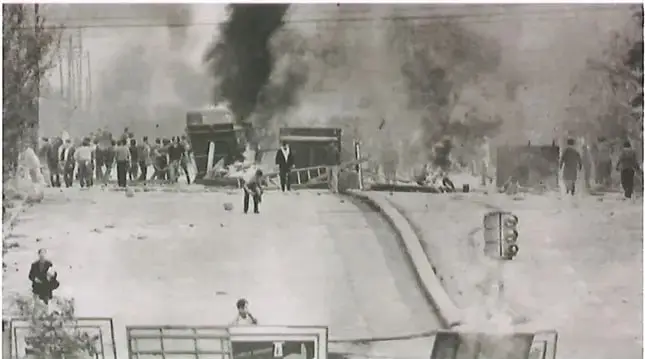 Fotografía histórica de una protesta o enfrentamiento urbano con humo, personas y obstáculos en una vía, relacionada con las movilizaciones populares de la época.