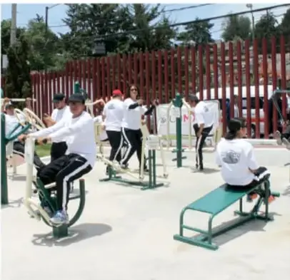 Foto de personas ejercitándose en aparatos de ejercicio al aire libre de un parque comunitario, con estructura de estación de ejercicio y usuarios en diferentes máquinas.