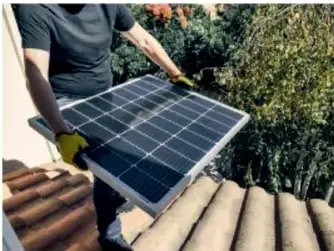 Persona con guantes que carga un panel solar fotovoltaico sobre un techo.