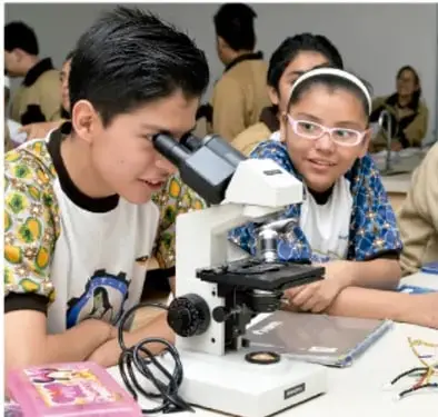 Fotografía de estudiantes de telesecundaria observando una muestra con un microscopio en el aula.