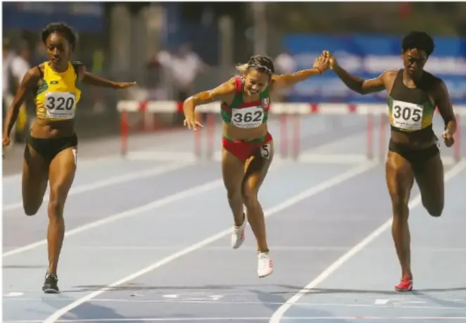 Fotografía de tres atletas femeninas cruzando la meta en una pista de atletismo, mostrando esfuerzo, competencia sana y compañerismo al darse la mano.