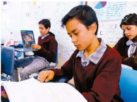 Estudiantes de telesecundaria trabajando con un libro y un proyector en el aula.
