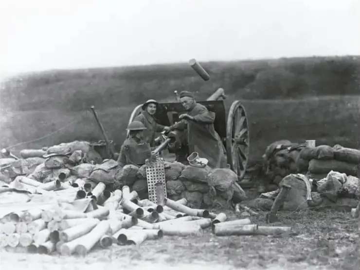 Fotografía histórica en blanco y negro de soldados operando un cañón junto a una enorme cantidad de casquillos y proyectiles usados, representando un campo de batalla de la Primera Guerra Mundial.