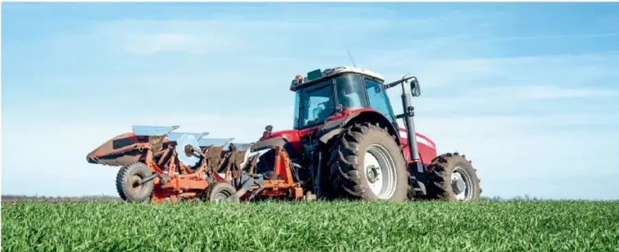 Fotografía de un tractor rojo trabajando en un campo agrícola verde bajo un cielo azul, ilustrando un sistema técnico aplicado a la agricultura.