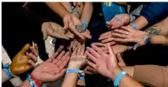 Grupo de manos unidas en círculo con pulseras de colores, símbolo de convivencia y comunidad.