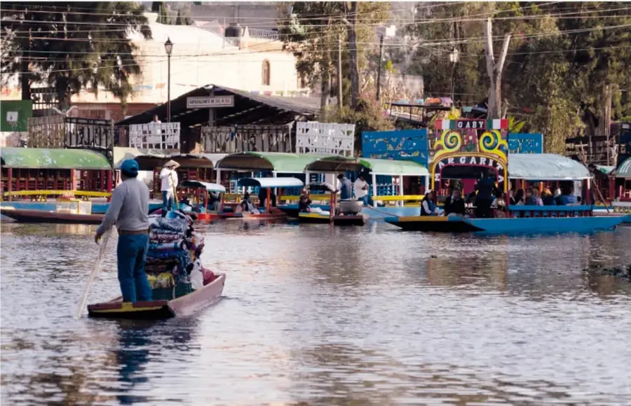Fotografía de un canal o lago con varias trajineras y personas navegando, escena típica de Xochimilco, México.