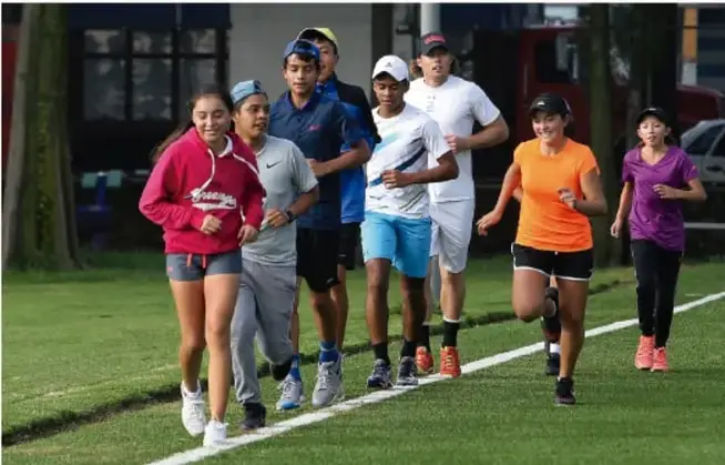 Fotografía de un grupo de adolescentes corriendo sobre el pasto en la escuela, ilustrando un juego de persecución durante el receso.