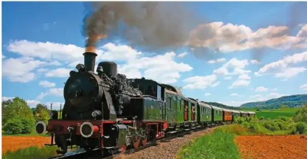 Fotografía de una locomotora de vapor antigua avanzando por el campo, con humo saliendo de su chimenea.