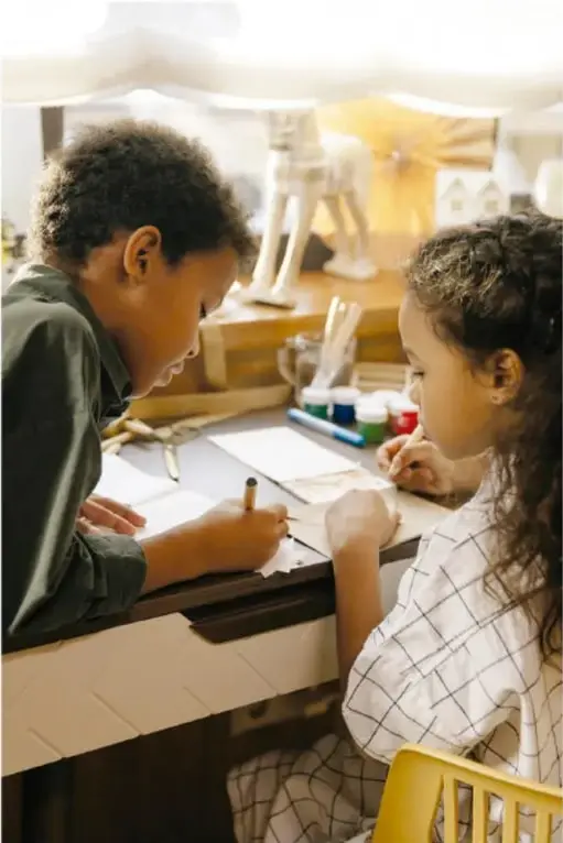 Dos estudiantes trabajando en una mesa con materiales escolares.