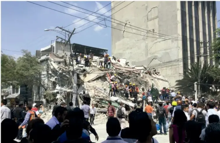 Fotografía de un edificio colapsado tras el sismo de 2017, con personas entre los escombros y una multitud observando.