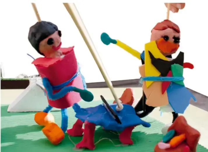 Fotografía de dos televisores de cartón decorados con figuras de plastilina y palitos de madera, sobre una base verde.