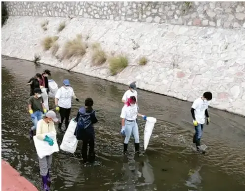 Fotografía de estudiantes con cubetas y redes recogiendo muestras o basura en un canal o escurrimiento de agua, actividad de trabajo comunitario.