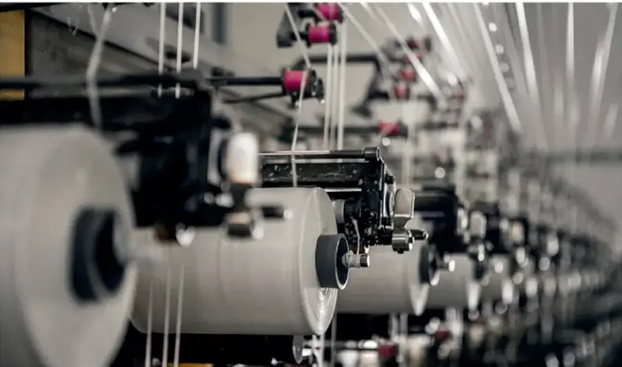 Maquinaria industrial con hilos y bobinas en una fábrica textil, representando la producción industrial y la posible generación de residuos.