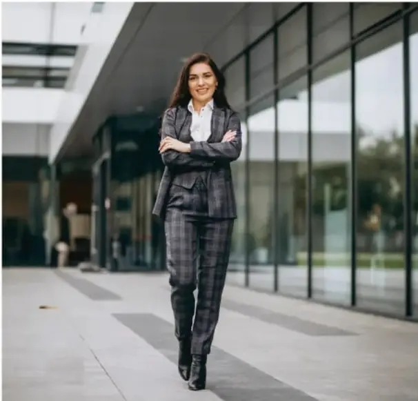 Fotografía de una mujer de negocios con traje a cuadros caminando frente a un edificio moderno de cristal, ilustrando el tema de emprendimiento.