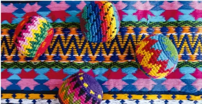 Fotografía de hilos de colores y textiles tradicionales con patrones geométricos y ovillos tejidos, representando la vestimenta y artesanía tradicional.