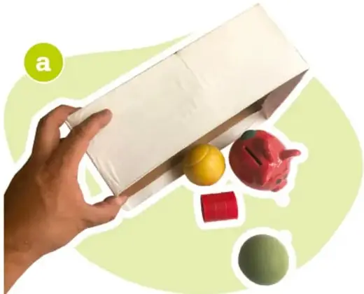 Manos vaciando una caja de cartón con objetos dentro (pelota, alcancía, cubo).