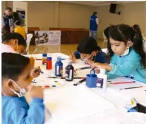 Niños y niñas en un aula trabajando con materiales escolares; una niña escribe y un niño observa.