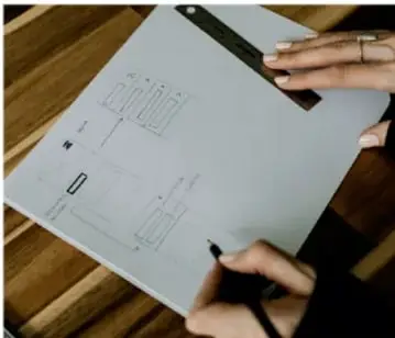 Fotografía de una persona dibujando con regla y marcador un esquema o diagrama sobre una hoja de papel, ilustrando la representación visual de información.