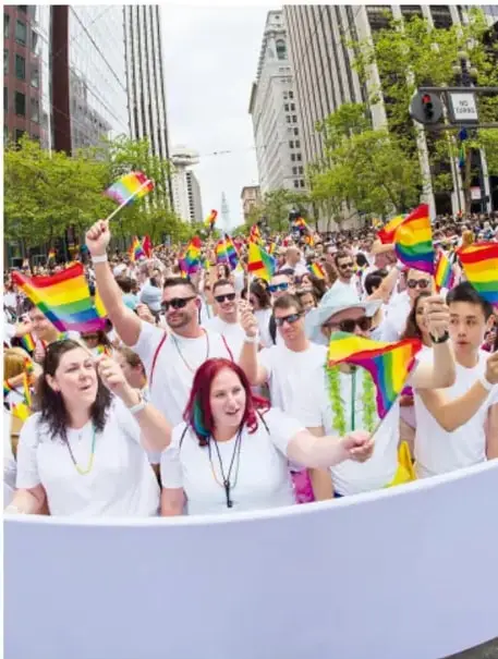 Marcha del orgullo LGBTTTIQ+ con personas ondeando banderas arcoíris en una avenida urbana.