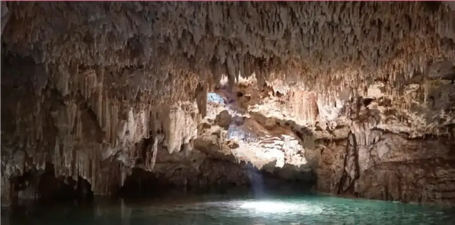 Fotografía del interior de una cueva con estalactitas y agua turquesa.