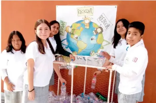 Fotografía de estudiantes de telesecundaria presentando un proyecto con cartel del planeta Tierra y botellas plásticas recolectadas para reciclar.