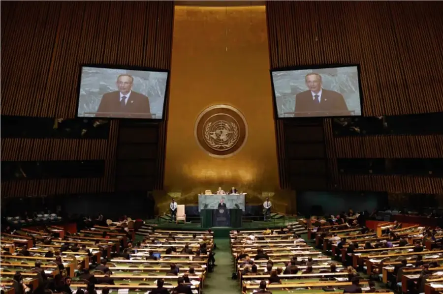 Fotografía del salón de la Asamblea General de la ONU con delegados sentados, pantallas que muestran a un orador y el emblema de la organización al centro.