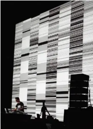 Fotografía en blanco y negro de una instalación sonora: una gran pared de franjas gráficas con una persona frente a equipo de audio.