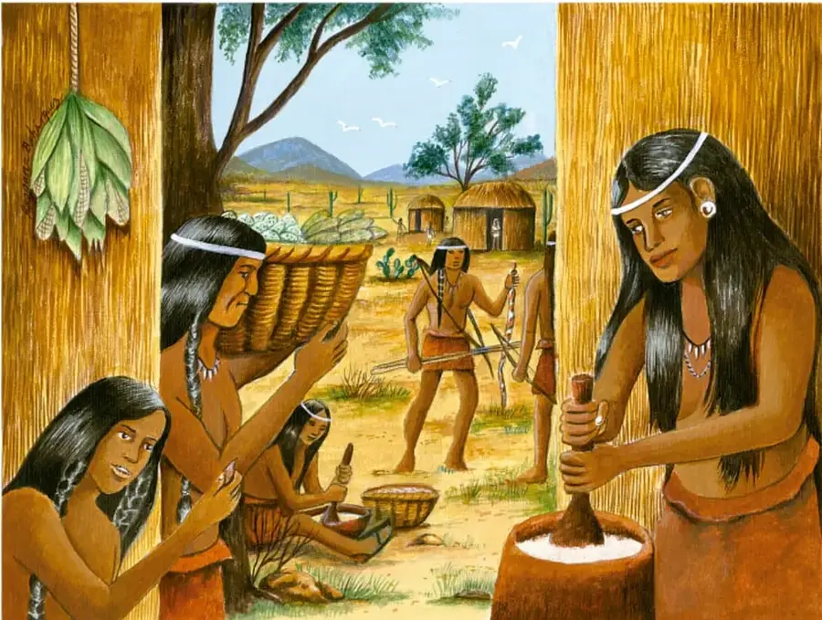 Ilustración de una aldea indígena: mujeres moliendo maíz con metate y molcajete, cestas, un hombre con arrocheladora, viviendas de jacal al fondo y paisaje desértico con magueyes y montañas.