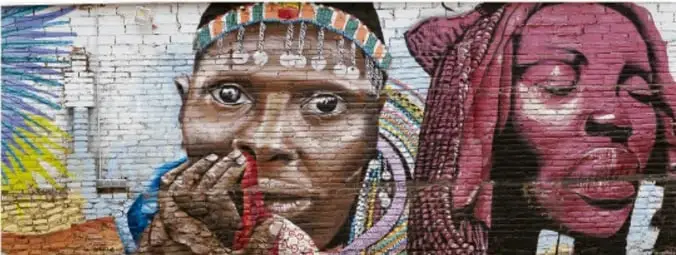 Mural o grafiti colorido en una pared de ladrillo que retrata el rostro de una mujer joven con turbante, ilustrando la expresión juvenil a través del arte urbano.