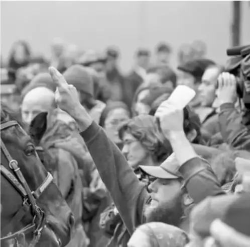 Fotografía en blanco y negro de una multitud en una manifestación o protesta, con personas levantando las manos y una pancarta.
