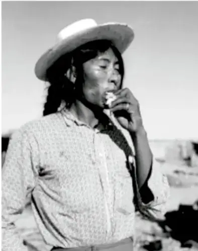 Fotografía en blanco y negro de una persona indígena con sombrero, de perfil, sosteniendo un objeto cerca de la boca.