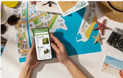 Manos sosteniendo un teléfono celular sobre un mapa y fotografías de viaje, representando el uso de las TIC en los servicios.
