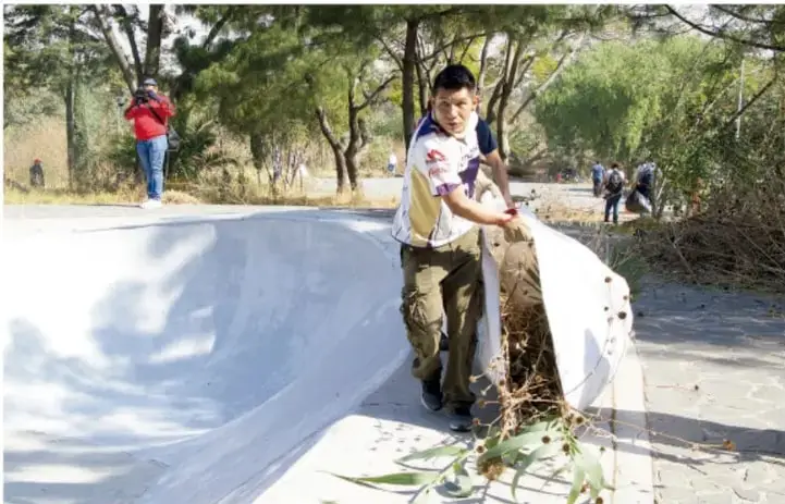 Fotografia de un nino recogiendo basura y ramas en un canal de concreto, acompanado de otras personas al fondo. Representa la participacion en la limpieza y mejora del entorno comunitario.