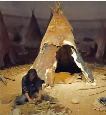 Fotografía de una vivienda neolítica de pieles o ramas, con una persona trabajando en el suelo, que ilustra el sedentarismo y las primeras aldeas.