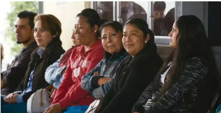 Fotografía de un grupo de personas de distintas edades sentadas en fila, atentas, probablemente participando en una asamblea o reunión comunitaria.