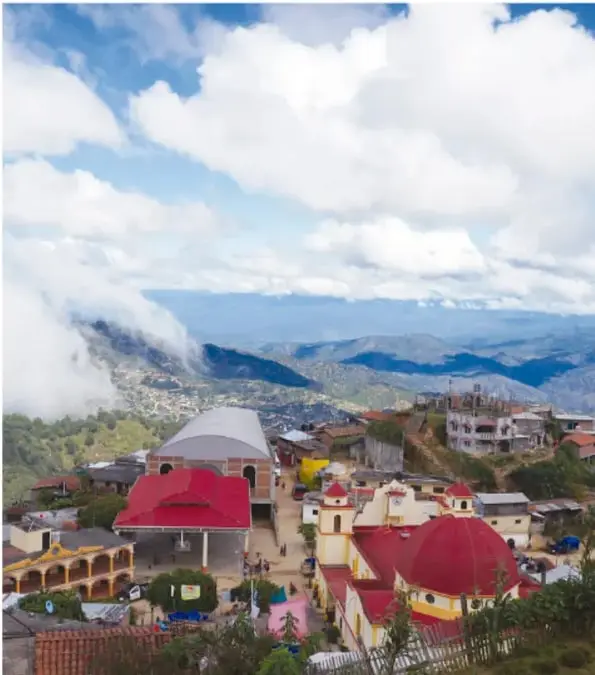 Vista panorámica de un pueblo de montaña con una iglesia de cúpula roja, casas y nubes sobre el valle; ilustra el tema de los lugares sagrados y la comunidad.