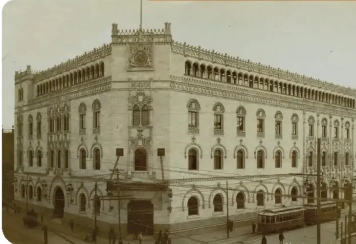 Litografía de la Casa de Correos en México, un edificio de estilo neoclásico inaugurado en 1907, con tranvías y personas en la calle.