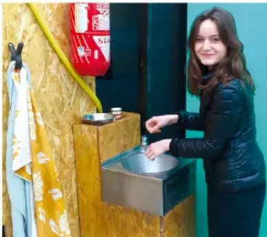 Una joven lavándose las manos en un lavabo, junto a un extintor y una toalla; ejemplifica los hábitos de higiene del cuidado personal.