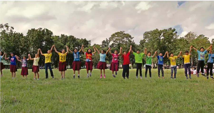 Fotografía de un grupo diverso de adolescentes tomados de las manos, saltando y celebrando en un parque con césped y árboles, ilustrando el sentido de pertenencia y la vida en comunidad.