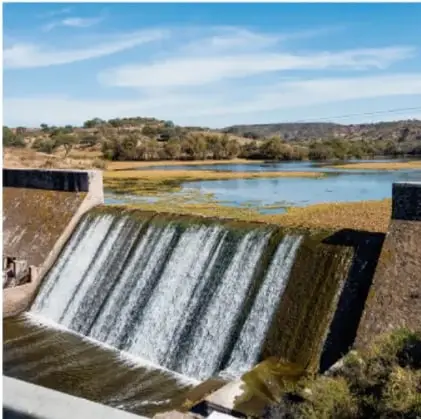 Fotografía de un azud o presa con agua cayendo por encima de la estructura en un paisaje natural.